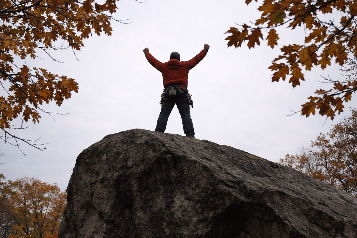 Climber standing on top of a boulder against an overcast autumn sky